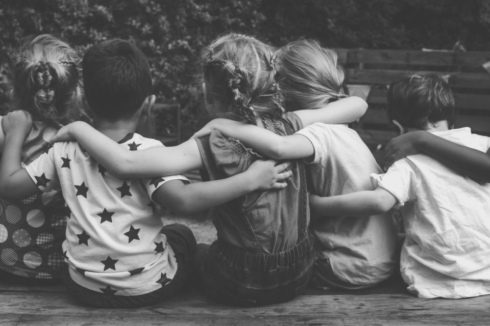 Psychological safety blog cover. Image is black & white and shows a group of kids facing away with their arms over each other's shoulders.