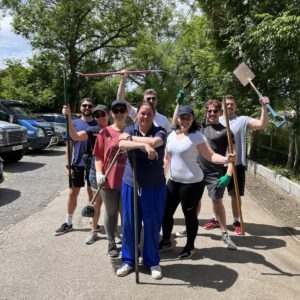 8 members of the revoco team standing in a triangle shape. Picture is of the team volunteering at Holly Hedge animal sanctuary. All of the team are holding tools, some of who are holding them in the air.