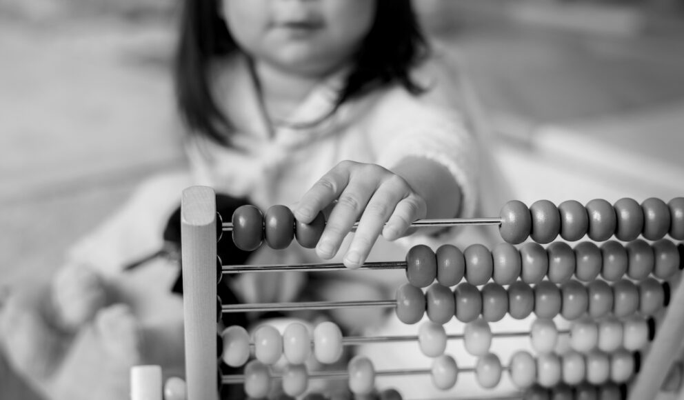 black and white close up photo of Little girl playing abacus for counting practice. Cover photo for IR35 blog.