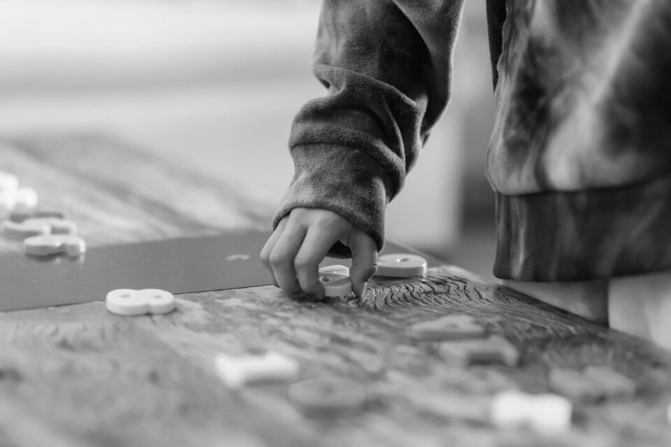 Black and white photo of a childs hand picking up plastic numbers from a wooden table. IMage is the cover image for the tech in numbers blog