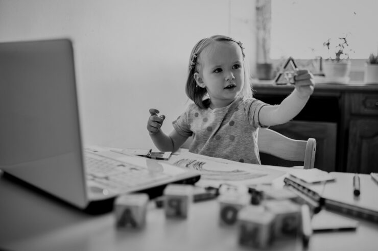 Black and white image of a Toddler girl learning shapes in front of laptop. Kid using computer to communicate with friends or kindergartners. Education or online communication for kids. Stay at home entertainment. Cover image for the programming languages blog.