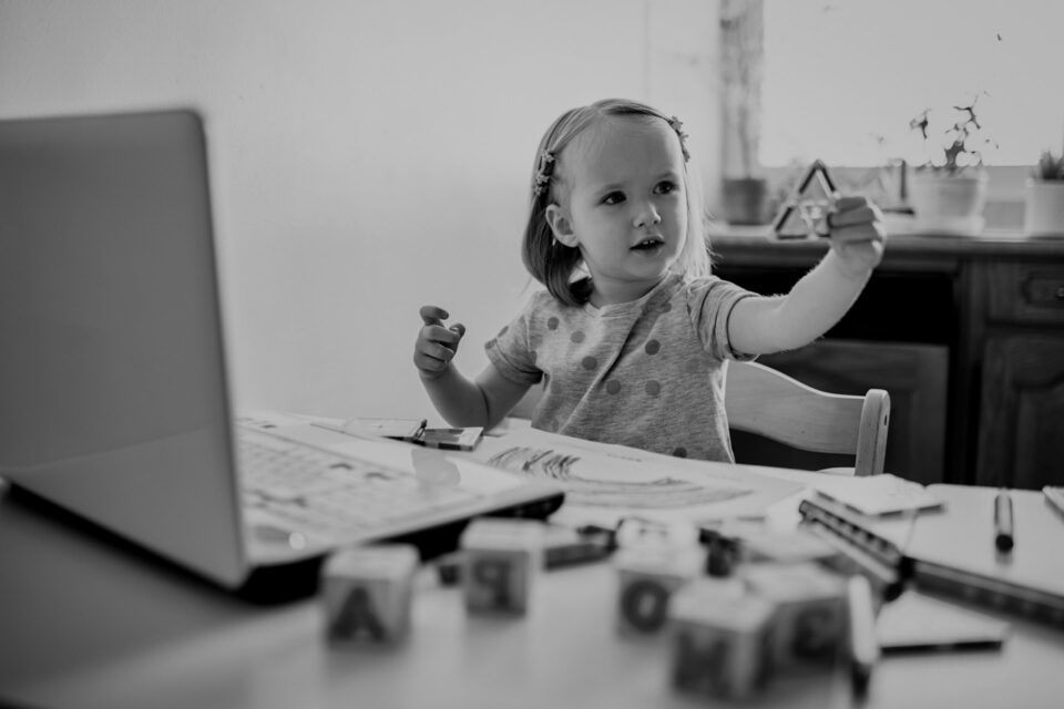 Black and white image of a Toddler girl learning shapes in front of laptop. Kid using computer to communicate with friends or kindergartners. Education or online communication for kids. Stay at home entertainment. Cover image for the programming languages blog.