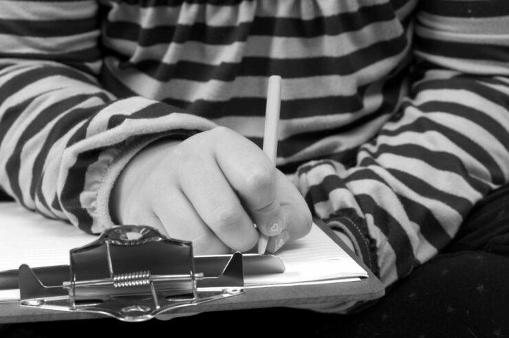 black and white close up image of a child writing on a clipboard. Cover image for the complete employee onboarding checklist blog.