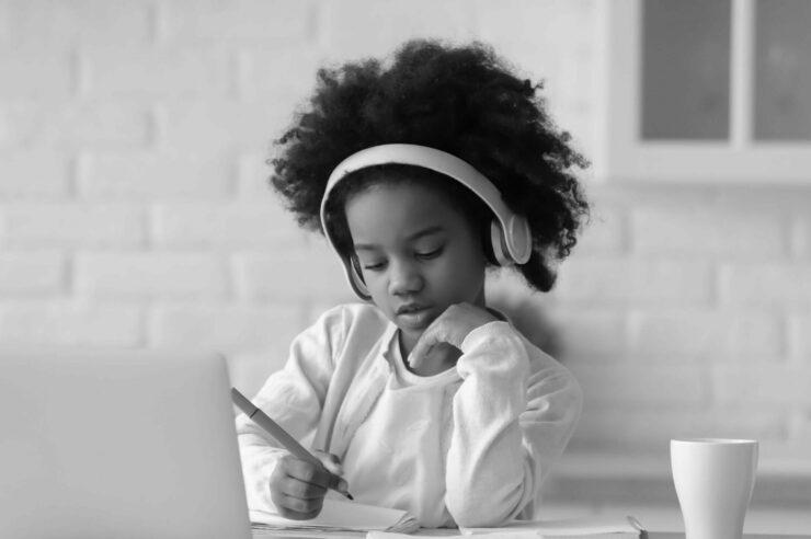 Black and white image of a girl writing down notes in front of a laptop. Cover image for the 'How to get more women into tech' blog