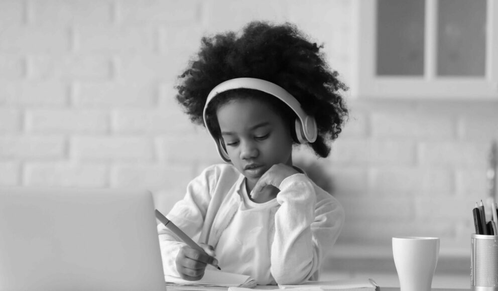 Black and white image of a girl writing down notes in front of a laptop. Cover image for the 'How to get more women into tech' blog