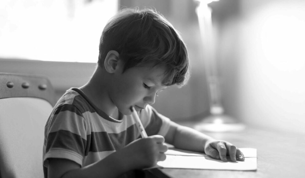 black and white image of a kid sat at a desk writing on a piece of paper. Image is a cover image for the 6 CV tips from recruiters blog image.