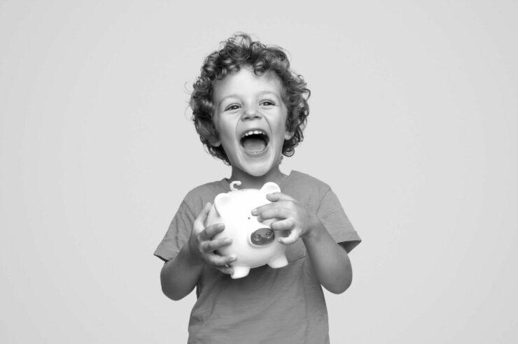 Black and white photo of a child excitedly holding a piggy bank. Cover image for revoco's 2023 uk tech salary guide.