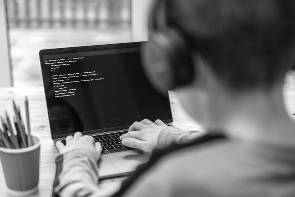 Black and white photo of a child on a laptop coding. Image is for the GCP vs AWS blog