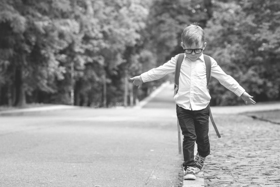 Black and white photo of a child walking on a curb on an empty street. He's got his arms out to help him balance. The photo is the cover image for Revoco's How to become a contractor blog
