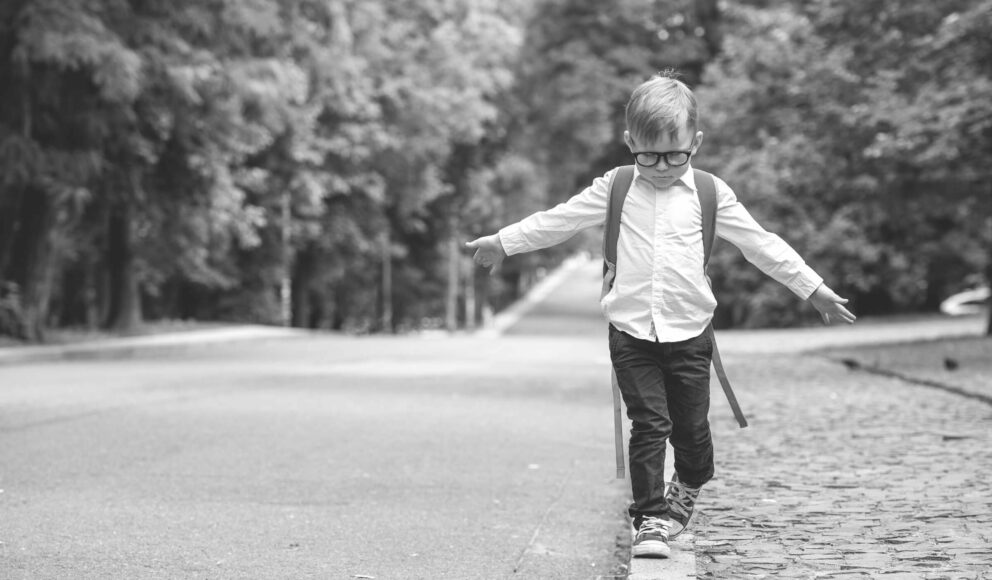 Black and white photo of a child walking on a curb on an empty street. He's got his arms out to help him balance. The photo is the cover image for Revoco's How to become a contractor blog
