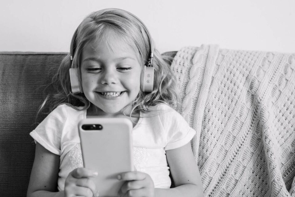 Black and white photo of a child sitting on the sofa watching something on her phone. Cover image for the social media job search blog.