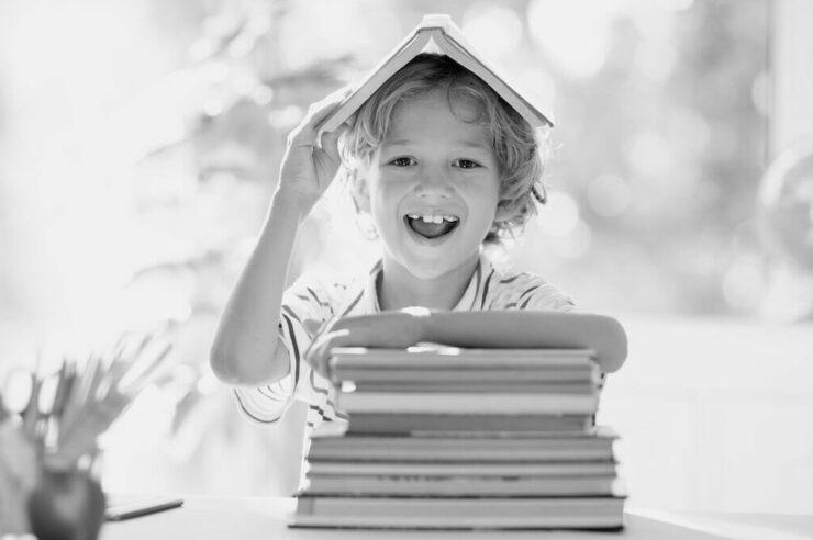 Black and white image of a kid sitting with a stack of books. Blog image for skills that make you more hireable in tech blog.