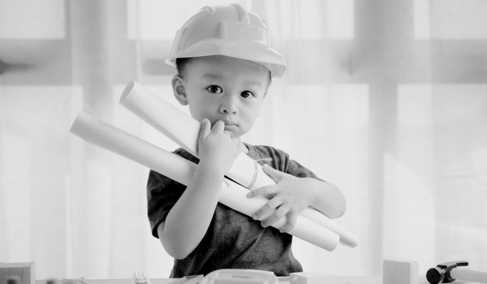 Black and white image of a child dressed as a builder holding building plans. Cover image for the contract worker blog.