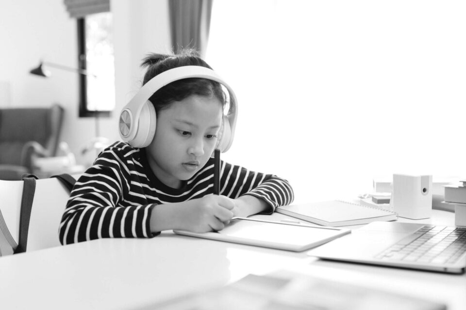 Black and white image of a child writing at her desk whilst wearing headphones. Cover image for the contractor onboarding checklist.